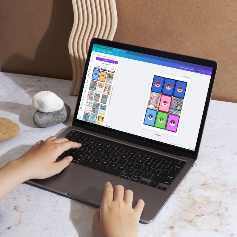 May include: A laptop computer with a white background and a screen displaying a design template with a grid of nine colorful squares. Each square contains a blue and white Pokeball graphic. The template is titled "Pokeball Card Layout".