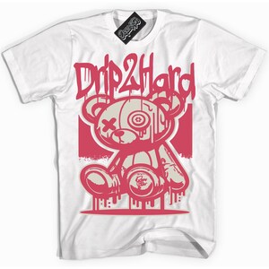 Könnte beinhalten: Weißes T-Shirt mit einer pinkfarbenen Grafik eines tropfenden Teddybären, der eine Spraydose hält. Der Text "Drip2Hard" befindet sich über dem Bären.