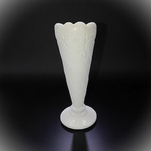 May include: A white, cone-shaped vase with a scalloped rim and a round base. The vase features a textured, swirling design and embossed floral patterns. The elegant, vintage-style vase is suitable for displaying flowers or as a decorative accent.