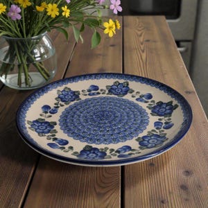 May include: Two ceramic plates with a blue floral design. The plates have a cream-colored background with a blue floral pattern around the edges and a detailed blue design in the center. The plates are on a wooden surface.