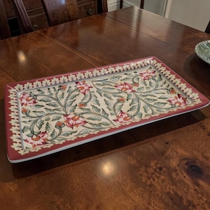 May include: Rectangular serving tray with a floral design. The tray has a cream-colored background with red and pink flowers and green leaves. The border is a deep red color.