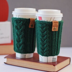 Puede incluir: Dos fundas de caf&eacute; de punto verde con etiquetas de cuero. Una etiqueta dice "Good Vibes Only" y la otra dice "Shhhhh...Good Coffee".