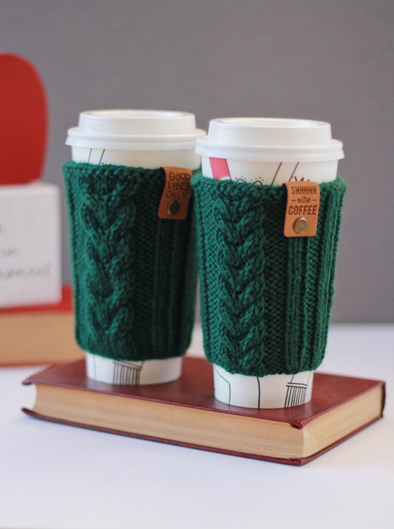 Puede incluir: Dos fundas de caf&eacute; de punto verde con etiquetas de cuero. Una etiqueta dice "Good Vibes Only" y la otra dice "Shhhhh...Good Coffee".