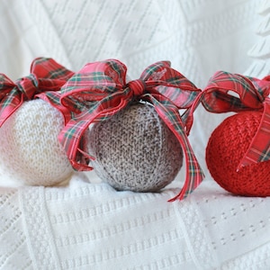 Puede incluir: Tres adornos navideños de punto con lazos de cinta a cuadros rojos y verdes. Los adornos son blancos, grises y rojos.