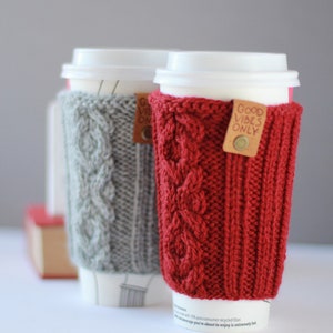 Puede incluir: Dos calentadores de taza de caf&eacute; de punto, uno gris y otro rojo, con el texto "Good Vibes Only" en el calentador rojo.