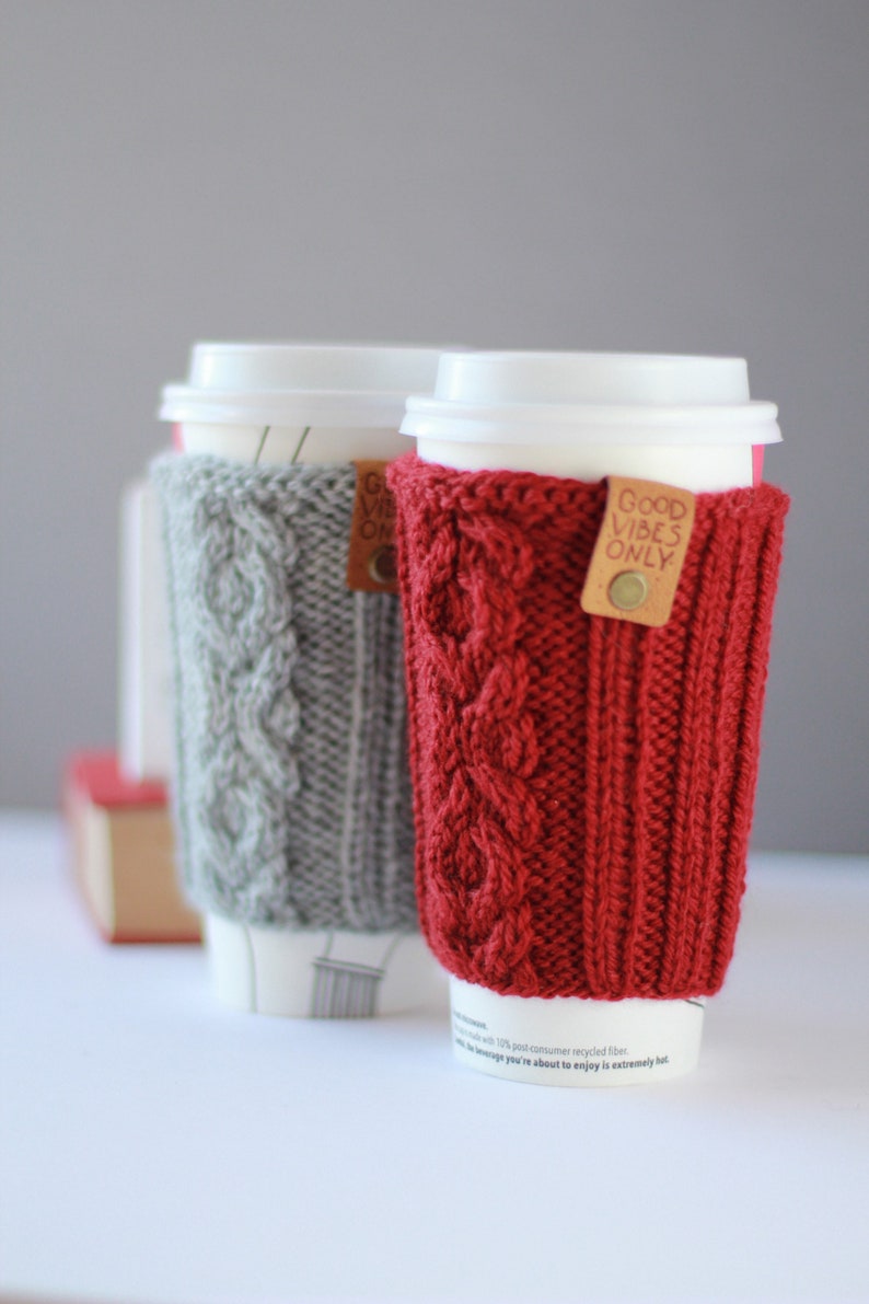 Puede incluir: Dos calentadores de taza de caf&eacute; de punto, uno gris y otro rojo, con el texto "Good Vibes Only" en el calentador rojo.