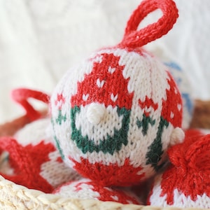 May include: A basket filled with knitted Christmas decorations. The decorations are red, white and green with a snowflake pattern.