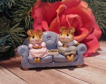 以下が含まれることがあります： ライトブルーのソファに座る2匹のネズミのミニチュアフィギュアセット。一匹はピンクのドレスを着てピンクのバラを持ち、もう一匹は白いシャツとグレーのズボンを着ています。お菓子の箱が2匹の間に置かれています。