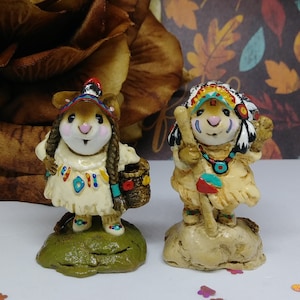 May include: Two decorative figurines of mice dressed in Native American attire. One mouse wears a headdress and holds a staff, while the other carries a basket. Both are on small bases, with detailed clothing and facial features.