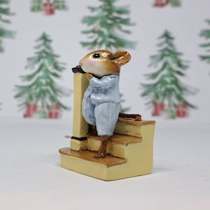 May include: A small figurine of a brown mouse with pink cheeks wearing light blue striped pajamas, standing on a set of yellow stairs with a matching yellow banister post. The mouse is positioned in profile, leaning against the post on the steps.