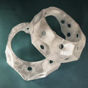 Puede incluir: Dos anillos de plástico blanco con un diseño geométrico y múltiples agujeros. Los anillos están apilados uno encima del otro.