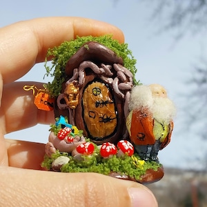 May include: A miniature clay house with a brown door and a moss roof. A small figure with a white beard and orange jacket stands next to the house. The house has a sign that says "home".