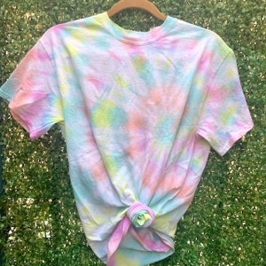 Puede incluir: Una camiseta tie-dye en tonos de rosa, azul, amarillo y verde. La camiseta está hecha de un material suave y cómodo y tiene un corte holgado.