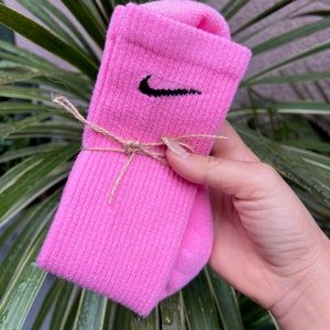 Puede incluir: Calcetines de deporte rosas con un logotipo de Nike negro en forma de swoosh.