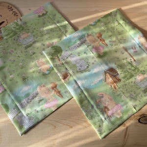 Könnte beinhalten: Zwei grüne Stoffquadrate mit einem weißen und rosa floralen Muster mit kleinen Tieren. Der Stoff hat einen dezenten Glanz und eine weiche Textur.