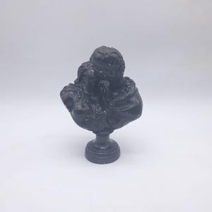 May include: A dark gray bust sculpture depicting two figures in a romantic embrace. The sculpture features detailed clothing and facial features, mounted on a round pedestal base. The bust is made of a solid material.