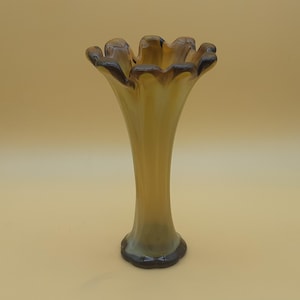 May include: An amber-coloured glass vase with a flared, ruffled rim. The vase has a slender, elongated body and a dark brown base. The rim has a dark brown trim. The vase is likely for decorative purposes.