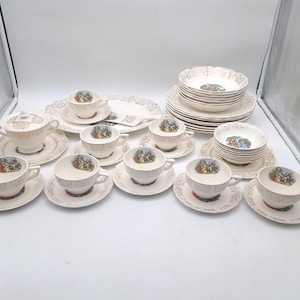 Puede incluir: Un juego de té vintage color crema con detalles de filigrana dorada. El juego incluye tazas, platillos, platos, cuencos, una azucarera y una fuente para servir. Cada pieza presenta una ilustración colorida.