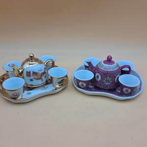 Peut inclure: Deux services à thé décoratifs en porcelaine. L'un présente une théière et des tasses bleu clair avec des accents dorés et un motif de dragon. L'autre a une théière et des tasses marron avec un motif floral. Les deux sont sur des plateaux assortis.