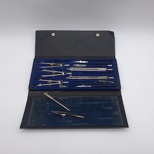 May include: A vintage drafting set in a black case. The set includes several silver-coloured compasses, dividers, and other drawing tools, neatly arranged on a blue velvet-lined interior. The case is open, revealing the tools, with a few loose pieces in the bottom.