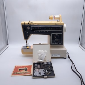 以下が含まれることがあります： クリームと黒のヴィンテージSinger Diana 560ミシン。ボビンと押え金が入ったクリーム色のアクセサリーケースと、Singer 560の取扱説明書が付属しています。ミシンには黒色の電源コードが付いています。