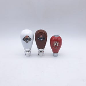 以下が含まれることがあります： 3つのビールタップハンドル。最初のものはRickard'sのロゴが入った白、2番目のものはRickard'sのロゴが入った茶色、3番目のものはAlexander Keith'sのロゴが入った赤です。すべて銀色のベースが付いています。