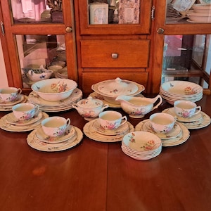 May include: A vintage porcelain tea set with floral designs. The set includes teacups, saucers, plates, bowls, a gravy boat, and a covered serving dish. The pieces are white with pink, yellow, and blue floral patterns.