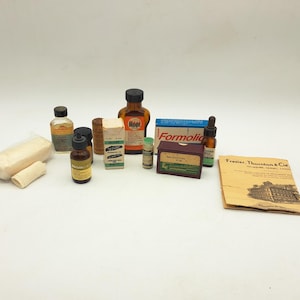 May include: A collection of vintage medical supplies including amber glass bottles with dropper caps, small cardboard boxes labelled Formolic and other text, two rolls of white gauze, and a tan paper pamphlet titled Frasier, Thornton & Cie.