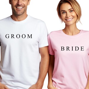 May include: A white t-shirt with the word "GROOM" printed on it and a pink t-shirt with the word "BRIDE" printed on it.