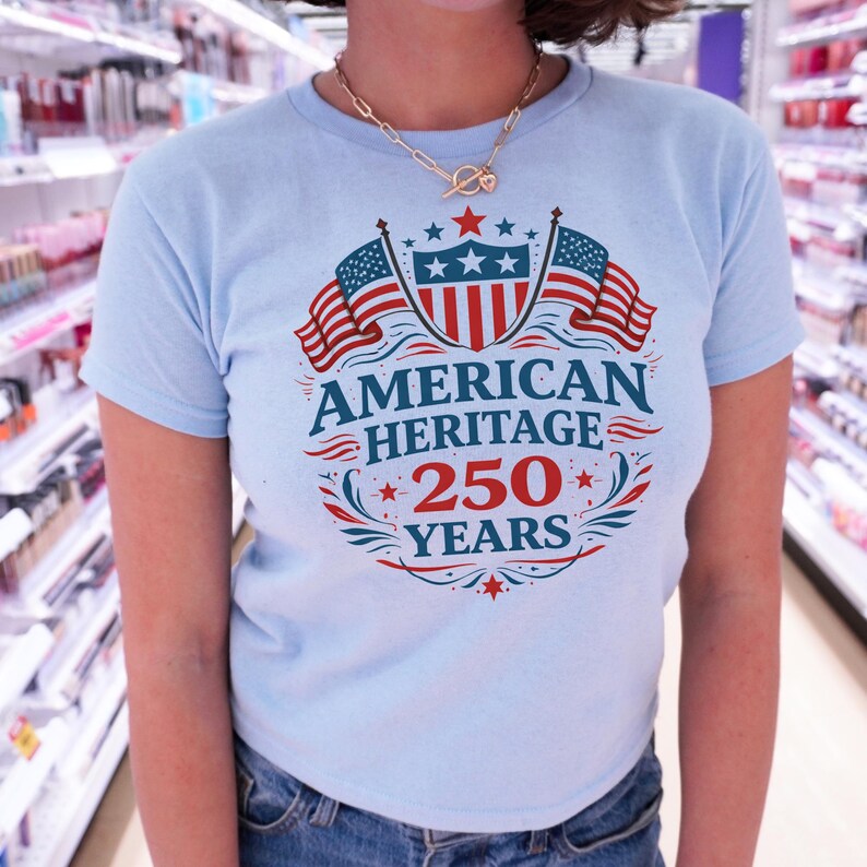 A person wearing a light blue t-shirt with a graphic design that says "American Heritage 250 Years" and features an American flag and stars.
