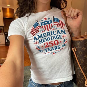 A person wearing a white t-shirt with a graphic design that says "American Heritage 250 Years" and an American flag.