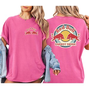 A woman wearing a pink t-shirt with the Red Bull logo and the text "Red Bull ENERGY DRINK" printed on it.