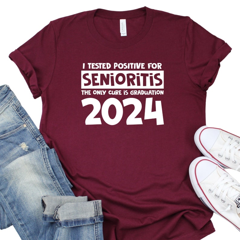 Op de afbeelding: Bordeauxkleurig T-shirt met witte tekst die luidt: "Ik ben positief getest op Senioritis. De enige remedie is afstuderen in 2024."