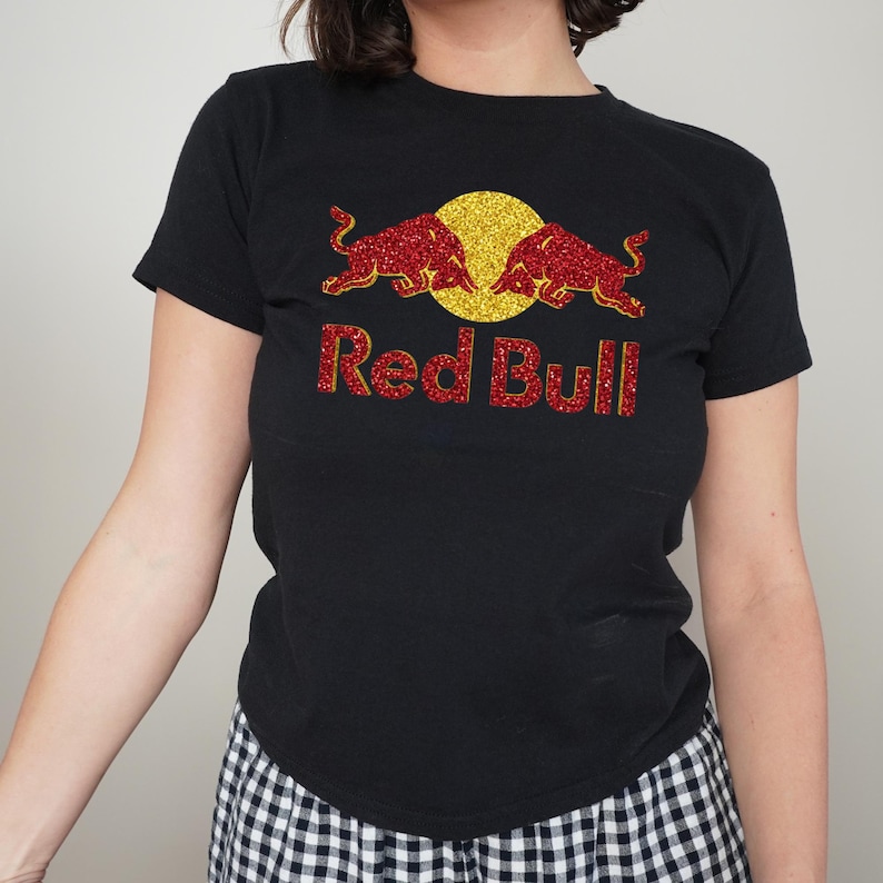 A person wearing a black t-shirt with a Red Bull logo and red glitter design.