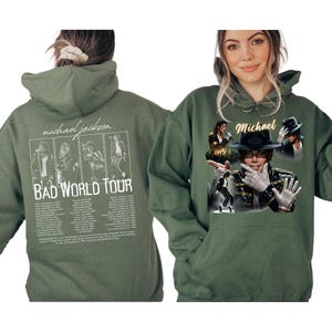 May include: Olive green hoodie featuring Michael Jackson. The front displays a collage of images and the name "Michael". The back has a graphic of Michael Jackson and the text "BAD WORLD TOUR".
