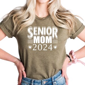 May include: A green t-shirt with the text "Senior Mom 2024" in white with two small hearts on either side of the year.
