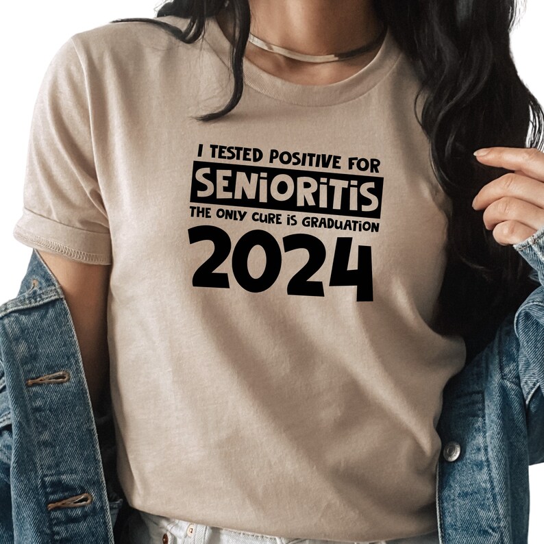 Op de afbeelding: Een beige T-shirt met zwarte tekst die luidt: "Ik heb positief getest op Senioritis. De enige remedie is afstuderen in 2024."
