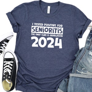 Op de afbeelding: Een marineblauw T-shirt met witte tekst die luidt: "Ik ben positief getest op Senioritis. De enige remedie is afstuderen in 2024".