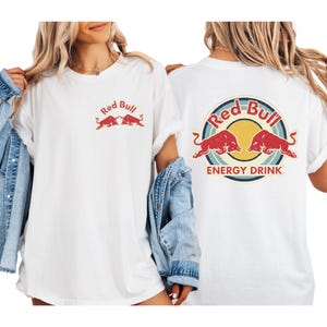 two women wearing white t-shirts with the Red Bull logo and the text "Red Bull Energy Drink" printed on them.