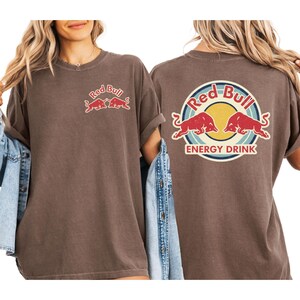 two women wearing brown t-shirts with the Red Bull logo and the text "Red Bull Energy Drink" printed on them.