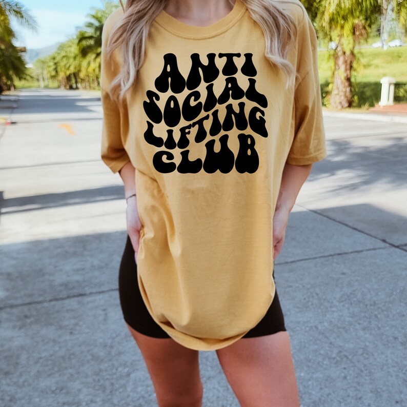 K&ouml;nnte beinhalten: Ein gelbes T-Shirt mit einer schwarzen Grafik, auf der in einer Retro-Schrift "Anti Social Lifting Club" steht.
