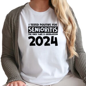 Op de afbeelding: Wit T-shirt met zwarte tekst die luidt: "Ik ben positief getest op Senioritis. De enige remedie is afstuderen in 2024."