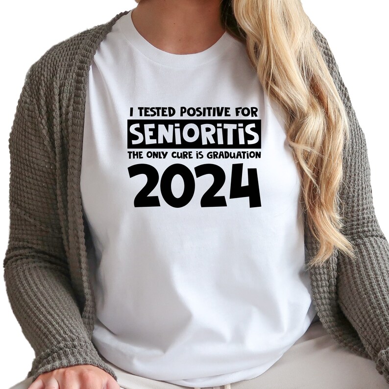 Op de afbeelding: Wit T-shirt met zwarte tekst die luidt: "Ik ben positief getest op Senioritis. De enige remedie is afstuderen in 2024."