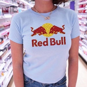 A woman wearing a light blue t-shirt with a Red Bull logo and red and gold glitter design.
