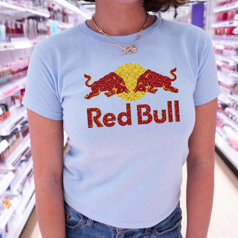 A woman wearing a light blue t-shirt with a Red Bull logo and red and gold glitter design.
