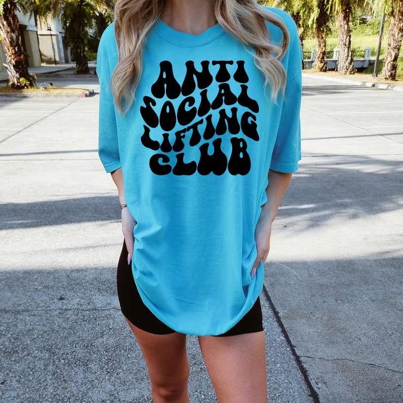 K&ouml;nnte beinhalten: Ein t&uuml;rkisfarbenes T-Shirt mit einer schwarzen Grafik, auf der in einer Retro-Schrift "Anti Social Lifting Club" steht.