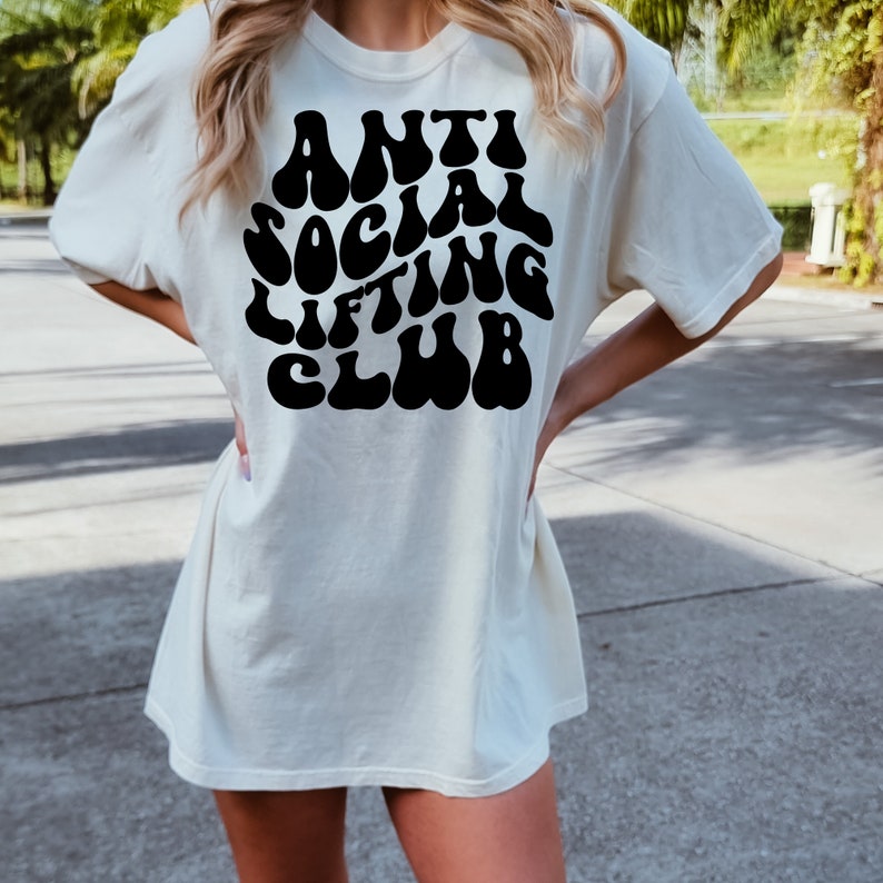 K&ouml;nnte beinhalten: Ein wei&szlig;es Oversize-T-Shirt mit einem schwarzen Grafikdruck, der "Anti Social Lifting Club" in einer Retro-Schriftart lautet.
