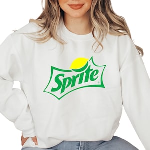 May include: White sweatshirt featuring the Sprite logo. The logo is green with a yellow lemon graphic. The word "Sprite" is in a green, stylized font. The sweatshirt is a casual, comfortable style.