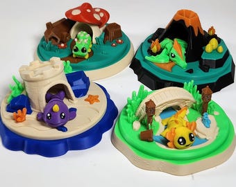 May include: Four 3D printed dioramas featuring small creatures: a green caterpillar by a red mushroom, a green dragon near a volcano, a purple narwhal in a sandcastle, and a yellow axolotl under a bridge with small lanterns.
