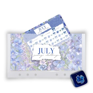 May include: A rectangular July savings challenge card with a blue floral pattern, featuring a torn paper overlay with the text July savings challenge, accompanied by a matching blue die with a single flower illustration on its top face.